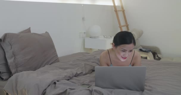 Temmelig glad asiatisk kvinde ved hjælp af bærbar computer i sengen – Stock-video