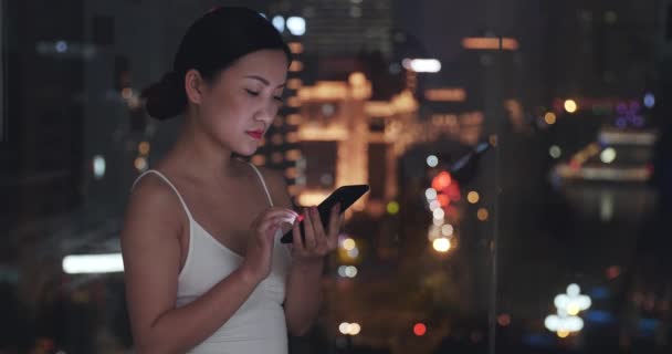 Mooie jonge aziatische vrouw met behulp van mobiele telefoon bij het raam 's nachts — Stockvideo