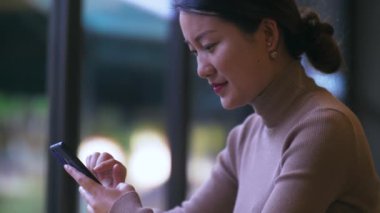 Kapalı alanda cep telefonu kullanan neşeli genç Çinli iş kadını