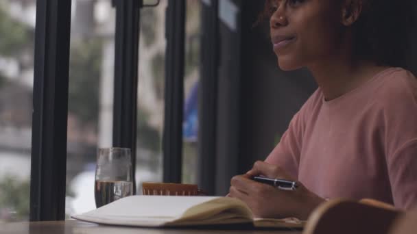 Jonge Afrikaanse vrouw schrijven in cafe door het raam — Stockvideo