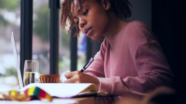 Junge afrikanische College-Studentin studiert Schreiben im Café — Stockvideo