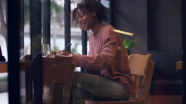 Vänsterhänt afrikansk ung kvinna skriver inomhus vid fönstret — Stockvideo