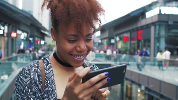 Gelukkig Afrikaans jong vrouw met behulp van mobiele telefoon in de straat — Stockvideo