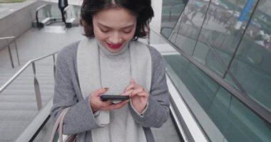 Şık ceketli güzel Asyalı kadın, yürüyen merdivene bin..