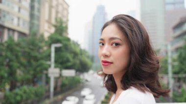Güzel genç Asyalı kadın dön ve kameraya bak ve şehir caddesinde gülümse sonra uzaklaş.