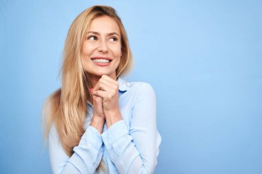 Mutlu görünümlü mutlu sarışın bir kadının portresi. Gülümseyen ve boş uzayda aşkla yan yana duran, el ele tutuşan, mavi stüdyoda izole bir hayat süren mutlu bir kadın.