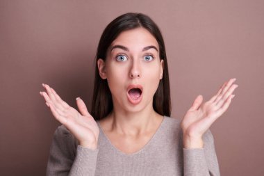 Kafkasyalı şoke olmuş esmer kız, ağzı açık, gözleri şişmiş, sıradan giyinmiş, inanılmaz haberler almış, kahverengi stüdyoda beklenmedik bir sürpriz hediye almış.