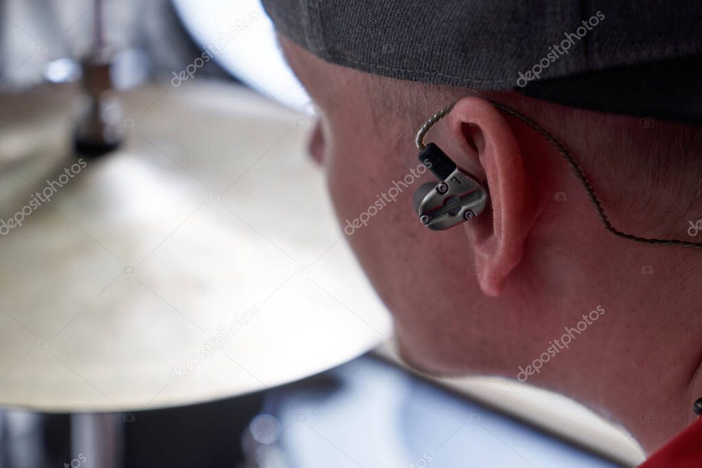 Drummer plays drum kit with a special in-ear intracanal earphone for musicians close-up 