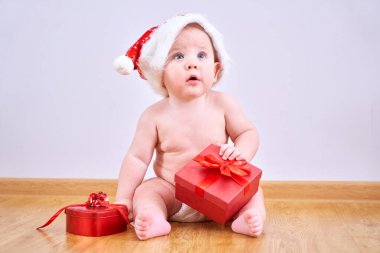 Noel Baba şapkalı, bebek bezi takan, kırmızı hediye kutulu komik çocuk yerde oturuyor, yeni yıla girmiş bebek ve hediyeler.
