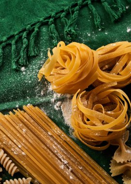 Yeşil kumaş arka planda değişik makarna çeşitleri, çeşitli makarna konsepti.