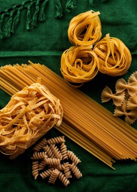 Yeşil kumaş arka planda değişik makarna çeşitleri, çeşitli makarna konsepti.