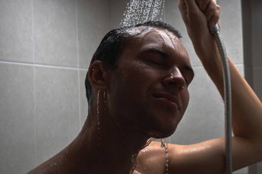 Genç yakışıklı adamın portresi kendini duş jeliyle yıkar, başını şampuanla yıkar.