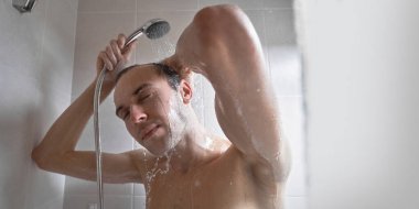 Genç yakışıklı adamın portresi kendini duş jeliyle yıkar, başını şampuanla yıkar.