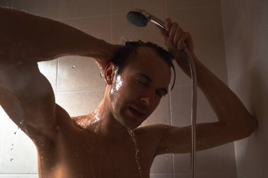 Genç yakışıklı adamın portresi kendini duş jeliyle yıkar, başını şampuanla yıkar.