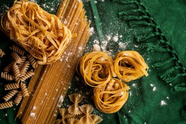 Yeşil kumaş arka planda değişik makarna çeşitleri, çeşitli makarna konsepti.