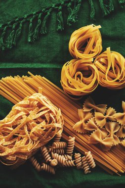 Yeşil kumaş arka planda değişik makarna çeşitleri, çeşitli makarna konsepti.
