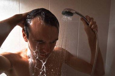 Genç yakışıklı adamın portresi kendini duş jeliyle yıkar, başını şampuanla yıkar.