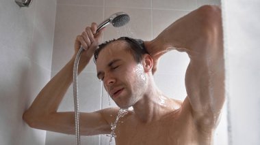 Genç yakışıklı adamın portresi kendini duş jeliyle yıkar, başını şampuanla yıkar.