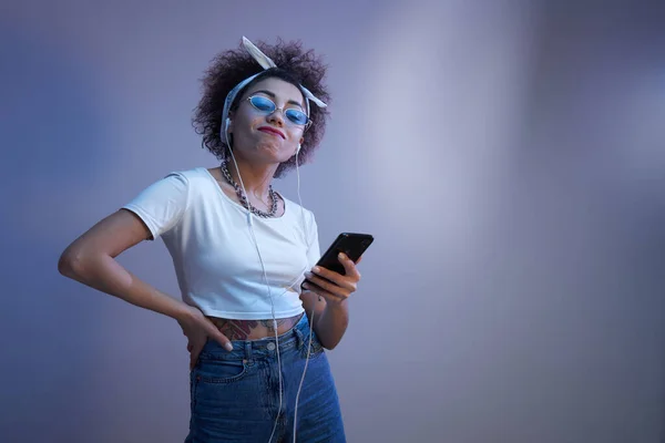 어슬렁 거리는 유행하는 소녀는 복제품 스튜디오 배경에 스마트폰 헤드폰을 — 스톡 사진