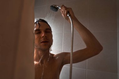 Genç yakışıklı adamın portresi kendini duş jeliyle yıkar, başını şampuanla yıkar.