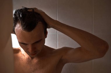 Genç yakışıklı adamın portresi kendini duş jeliyle yıkar, başını şampuanla yıkar.