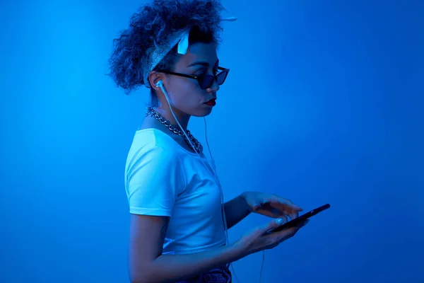 어슬렁거리는 유행하는 소녀는 녹음실 배경에 스마트폰 이어폰을 사용하여 온라인 음악을 — 스톡 사진