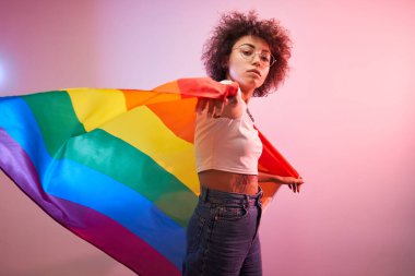 Igbtq konsepti. Stüdyoda izole edilmiş gökkuşağı bayrağı tutan kıvırcık saçlı pozitif beyaz kız.
