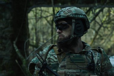 Ormanda makineli tüfekle profesyonel ekipman içinde uçan yumuşak oyuncunun portresi. Savaşta silahlı bir asker