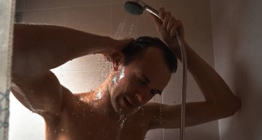 Genç yakışıklı adamın portresi kendini duş jeliyle yıkar, başını şampuanla yıkar.