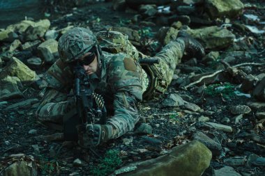 Profesyonel ekipmanlı, kasklı, havalı oyuncunun portresi ormanda silahla kurbana nişan alıyor. Savaşta silahlı bir asker