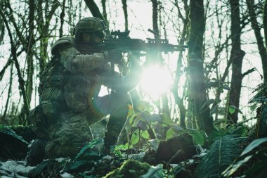 Profesyonel ekipmanlı, kasklı, havalı oyuncunun portresi ormanda silahla kurbana nişan alıyor. Savaşta silahlı bir asker