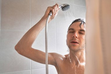 Genç yakışıklı adamın portresi kendini duş jeliyle yıkar, başını şampuanla yıkar.