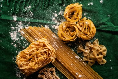 Yeşil kumaş arka planda değişik makarna çeşitleri, çeşitli makarna konsepti.