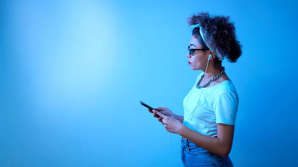 Trendy Girl Afro Curls Uses Smartphone Earphones Blue Studio Background — Stock Photo, Image
