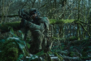 Profesyonel ekipmanlı, kasklı, havalı oyuncunun portresi ormanda silahla kurbana nişan alıyor. Savaşta silahlı bir asker