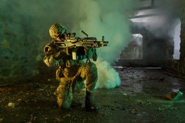 Terk edilmiş binada makineli tüfekle profesyonel ekipman içinde havalı oyuncunun portresi. Savaşta sisli ve dumanlı silahlı asker