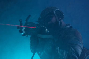 Terk edilmiş binada makineli tüfekle profesyonel ekipman içinde havalı oyuncunun portresi. Savaşta sisli ve dumanlı silahlı asker