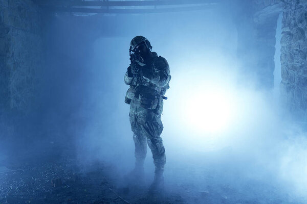 Portrait of airsoft player in professional equipment with machine gun in abandoned ruined building. Soldier with weapons at war in smoke and fog