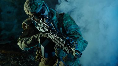 Terk edilmiş binada makineli tüfekle profesyonel ekipman içinde havalı oyuncunun portresi. Savaşta sisli ve dumanlı silahlı asker