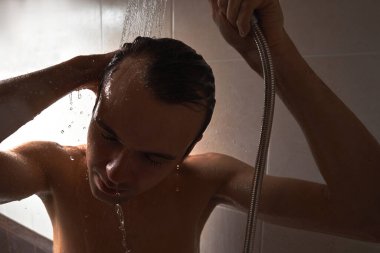 Genç yakışıklı adamın portresi kendini duş jeliyle yıkar, başını şampuanla yıkar.