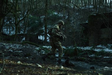 Ormanda makineli tüfekle profesyonel ekipman içinde uçan yumuşak oyuncunun portresi. Savaşta silahlı bir asker