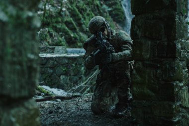 Profesyonel ekipmanlı, kasklı, havalı oyuncunun portresi ormanda silahla kurbana nişan alıyor. Savaşta silahlı bir asker