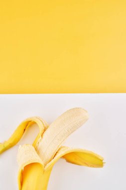 Sarı arkaplanda yarı soyulmuş muz ve kopyalama alanı