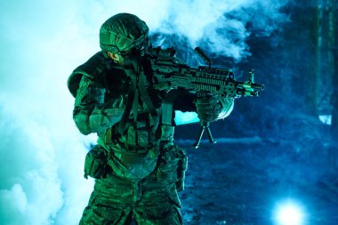 Terk edilmiş binada makineli tüfekle profesyonel ekipman içinde havalı oyuncunun portresi. Savaşta sisli ve dumanlı silahlı asker