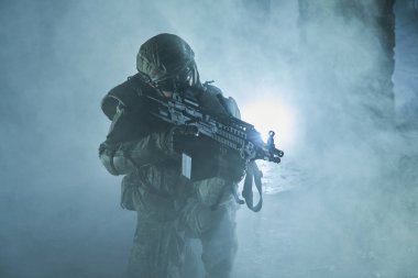 Terk edilmiş binada makineli tüfekle profesyonel ekipman içinde havalı oyuncunun portresi. Savaşta sisli ve dumanlı silahlı asker