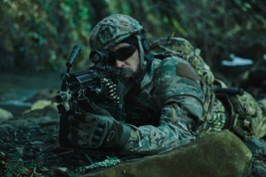 Profesyonel ekipmanlı, kasklı, havalı oyuncunun portresi ormanda silahla kurbana nişan alıyor. Savaşta silahlı bir asker