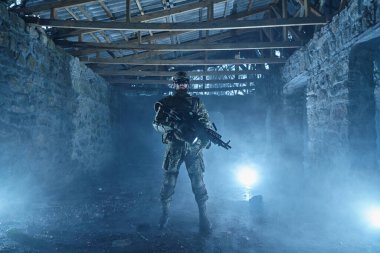 Terk edilmiş binada makineli tüfekle profesyonel ekipman içinde havalı oyuncunun portresi. Savaşta silahlı bir asker