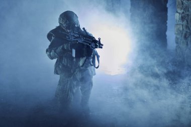 Terk edilmiş binada makineli tüfekle profesyonel ekipman içinde havalı oyuncunun portresi. Savaşta sisli ve dumanlı silahlı asker
