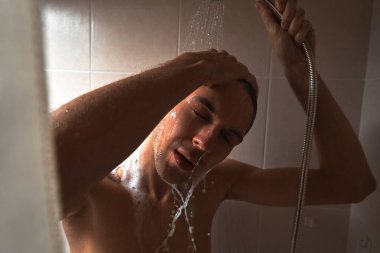 Genç yakışıklı adamın portresi kendini duş jeliyle yıkar, başını şampuanla yıkar.