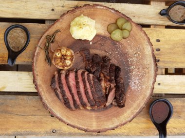 Ahşap bir tahtanın üzerinde orta pişmiş biftek, sos ve tuz.